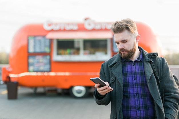 Retrato de hombre joven guapo con smartphone de pie delante del camión de comida