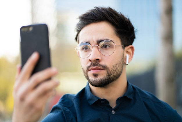 Retrato de hombre joven con identificación facial para desbloquear el teléfono móvil mientras está de pie al aire libre.