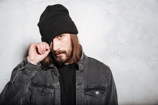 Retrato de un hombre joven inconformista con barba posando y mirando al frente aislado sobre la pared