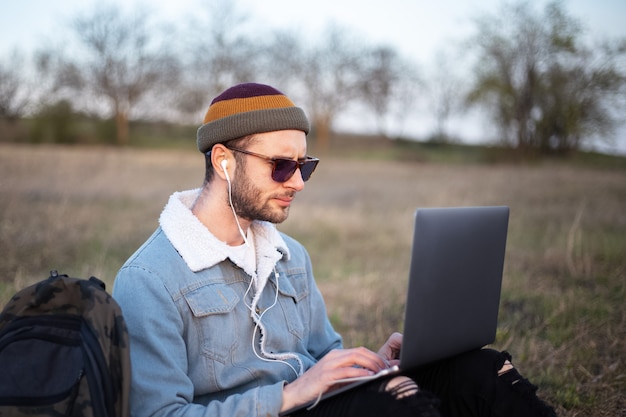 Retrato de hombre joven inconformista usando laptop al aire libre