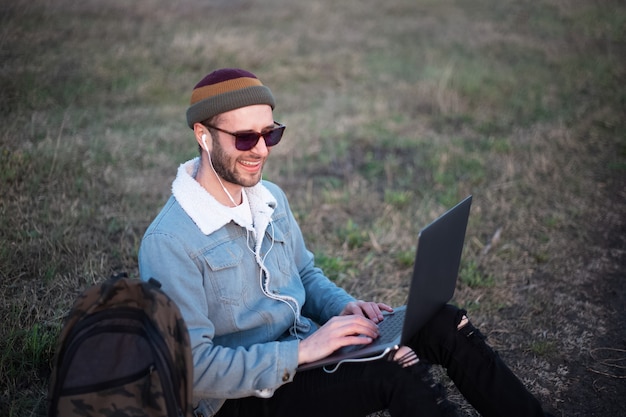 Retrato de hombre joven inconformista usando laptop al aire libre