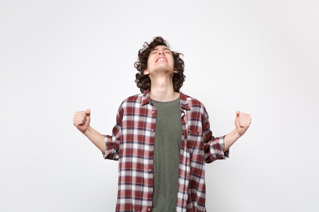 Foto retrato de hombre joven lleno de alegría en ropa casual mirando hacia arriba, diciendo que sí, apretando los puños como ganador aislado sobre fondo de pared blanca. personas sinceras emociones, concepto de estilo de vida. simulacros de espacio de copia.