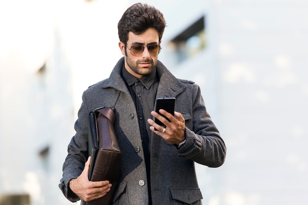Retrato de hombre joven moderno con su teléfono móvil en la calle.