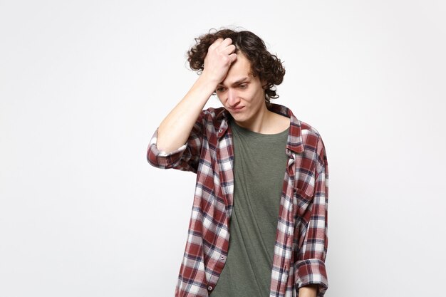 Foto retrato de hombre joven molesto preocupado en ropa casual mirando hacia abajo poniendo la mano en la cabeza aislada sobre fondo de pared blanca en estudio. personas sinceras emociones, concepto de estilo de vida. simulacros de espacio de copia.