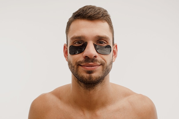 Retrato de hombre joven con parche en el ojo en la cara. Chico barbudo europeo sonriente con una piel perfecta mirando a la cámara. Concepto de cuidado de la piel de la cara. Aislado sobre fondo blanco. Sesión de estudio. Copia espacio