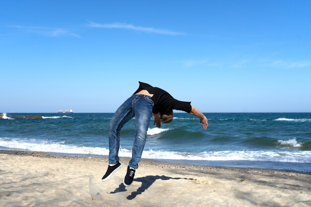 Retrato de hombre joven parkour haciendo flip o voltereta en la playa. Momento congelado de flip.