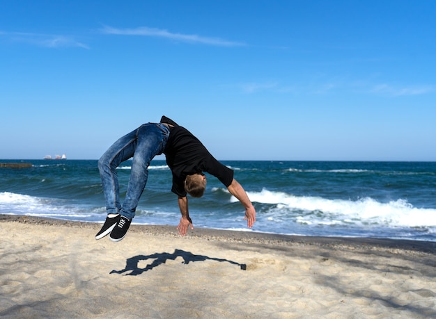 Retrato de hombre joven parkour haciendo flip o voltereta en la playa
