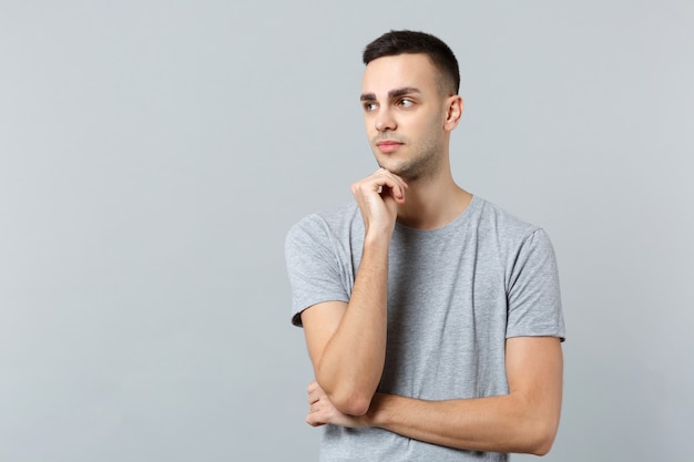 Retrato de hombre joven pensativo en ropa casual mirando a un lado y poner la mano apuntando hacia arriba en la barbilla