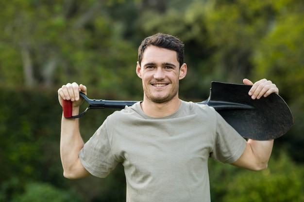 Retrato de hombre joven de pie en el jardín con una pala de jardinería