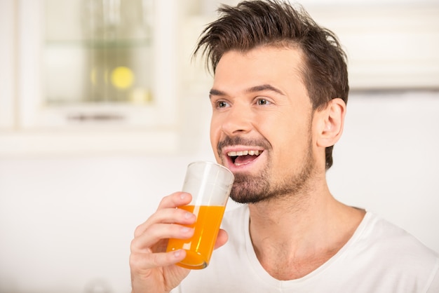 Retrato de un hombre joven que está bebiendo el jugo en cocina.