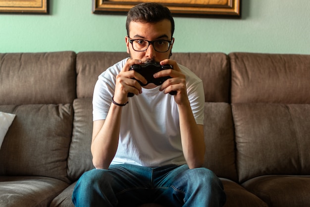 Retrato del hombre joven que juega al videojuego que sostiene el control inalámbrico en su hogar.