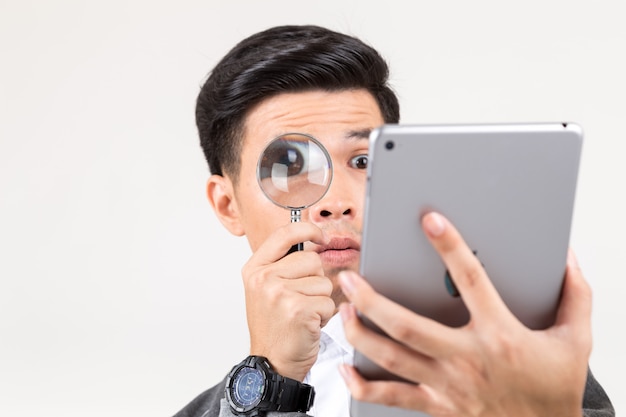 Retrato de un hombre joven que sostiene la lupa para leer la tableta.