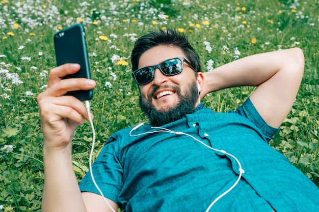 Retrato de hombre joven relajándose en la hierba y con smartphone
