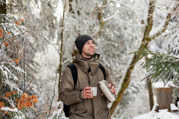 Retrato de hombre joven en ropa de abrigo en el bosque de invierno Bebiendo té caliente al aire libre del termo Senderismo Turismo