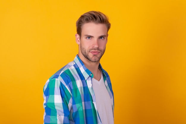 Retrato de hombre joven serio en camisa a cuadros fondo amarillo guapo