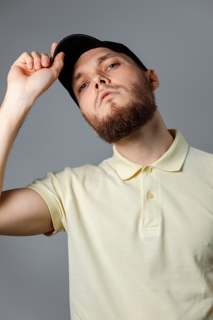 Retrato de hombre joven serio en una camiseta amarilla y gorra negra sobre gris.