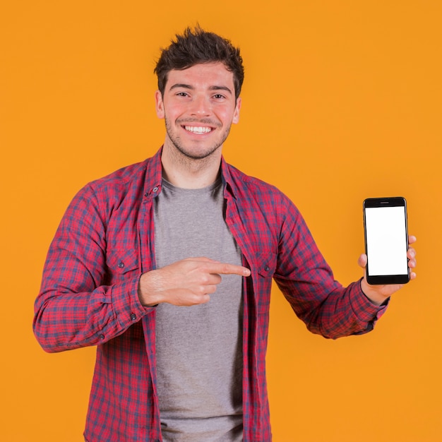 Foto retrato de un hombre joven sonriente que muestra su teléfono móvil contra un telón de fondo naranja