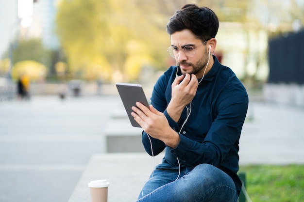 Retrato de hombre joven con tableta digital mientras está sentado en un banco al aire libre. Concepto urbano.