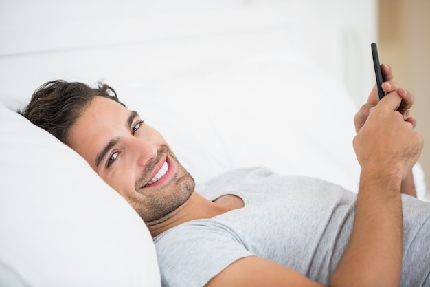 Retrato de hombre joven con teléfono móvil en la cama