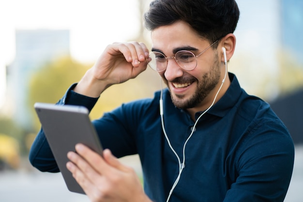 Retrato de hombre joven con una videollamada en tableta digital mientras está parado en un banco al aire libre