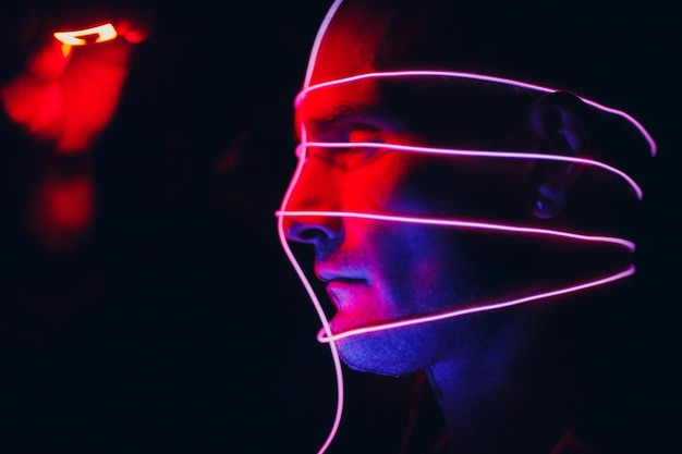 Retrato de hombre con líneas de tubos de neón en la cara en la oscuridad Concept cyberpunk y realidad virtual