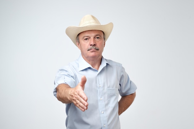 Retrato de un hombre maduro americano serio con sombrero de vaquero estirando la mano para sacudir para dar la bienvenida a alguien