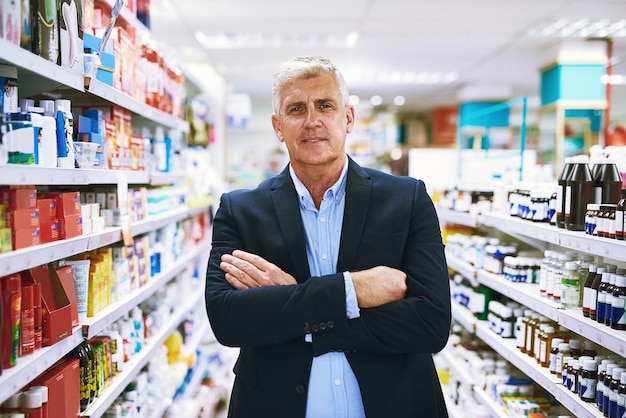 Retrato de hombre maduro y brazos plegados en una farmacia con dueño de un pequeño negocio en una tienda de atención médica y bienestar Confidencia farmacia y empresario con orgullo del éxito de la tienda en el estante de la farmacia
