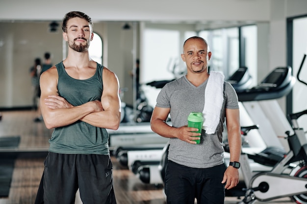 Retrato de hombre maduro cansado de razas mixtas y pround sonriente preparador físico de pie en el gimnasio después del entrenamiento