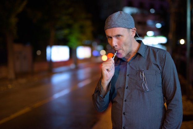 Retrato de hombre maduro, fumar cigarrillo electrónico en las calles por la noche