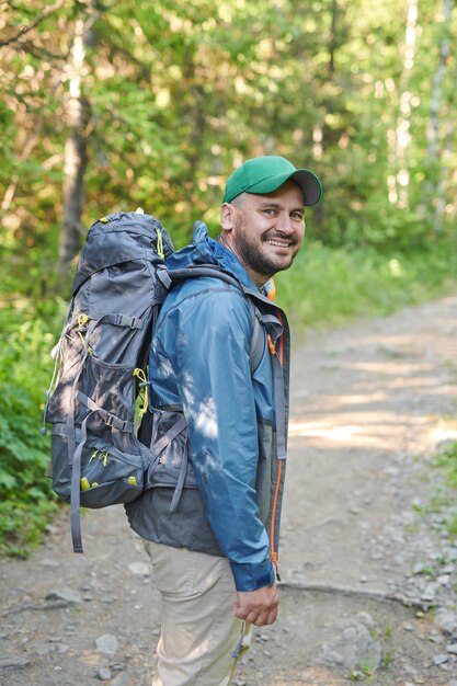 Retrato de hombre maduro con mochila sonriendo a la cámara mientras camina en el bosque