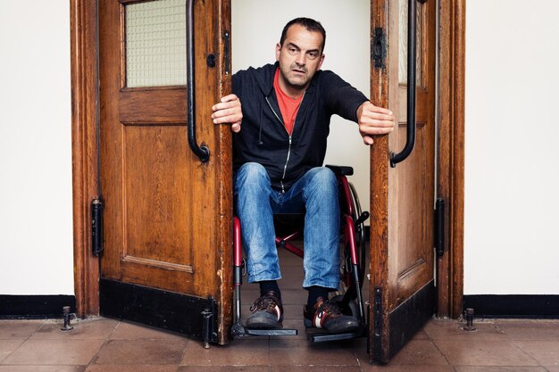 Foto retrato de un hombre maduro sentado en una silla de ruedas abriendo la puerta