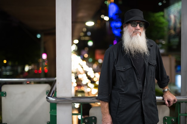 Retrato de hombre maduro turista barbudo explorando las calles de la ciudad de Bangkok, Tailandia en la noche