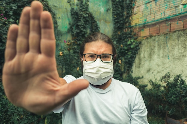 Foto retrato de un hombre con una máscara contra la gripe haciendo gestos para detenerse al aire libre