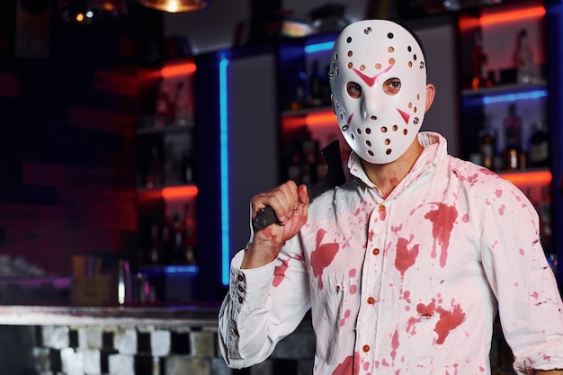 Retrato de hombre con máscara de hockey que se encuentra en la fiesta temática de halloween con maquillaje y disfraz de miedo.