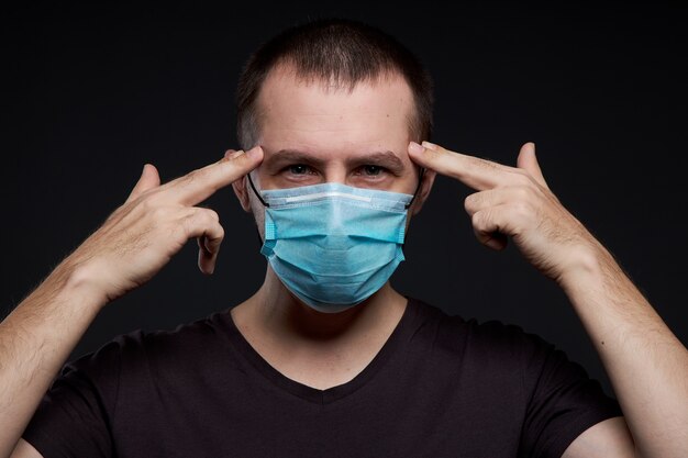 Retrato de un hombre con una máscara médica sobre un fondo oscuro, una infección por coronavirus