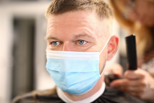 Retrato de hombre con máscara protectora médica que se corta en peluquería.