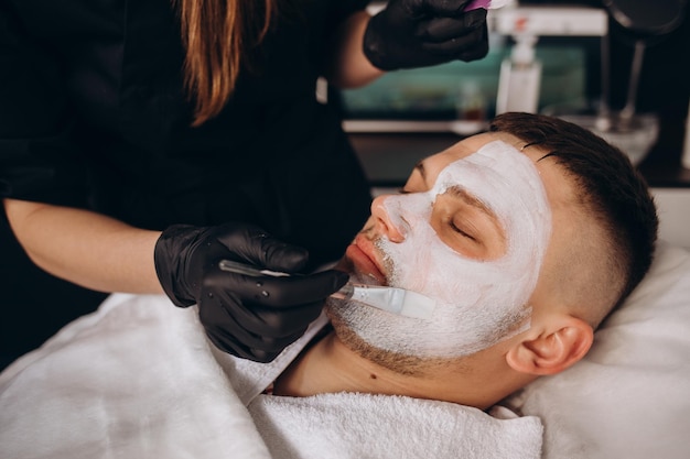 Foto retrato de hombre con mascarilla facial de arcilla en spa de belleza