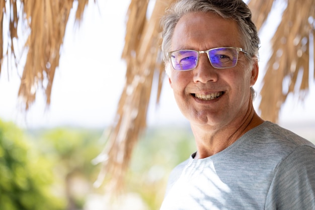 Retrato de un hombre mayor caucásico sonriente con anteojos de pie en un centro turístico en verano. Concepto inalterado, jubilación, vacaciones, disfrute, playa, feliz y estilo de vida.