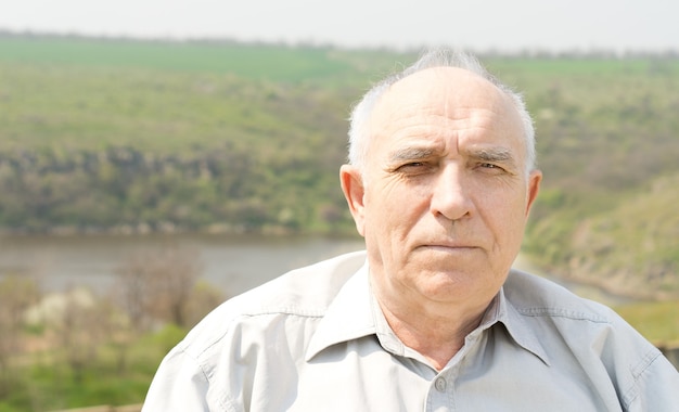 Retrato de un hombre mayor de pelo gris calvo en el sol de verano con un valle y un lago en el fondo