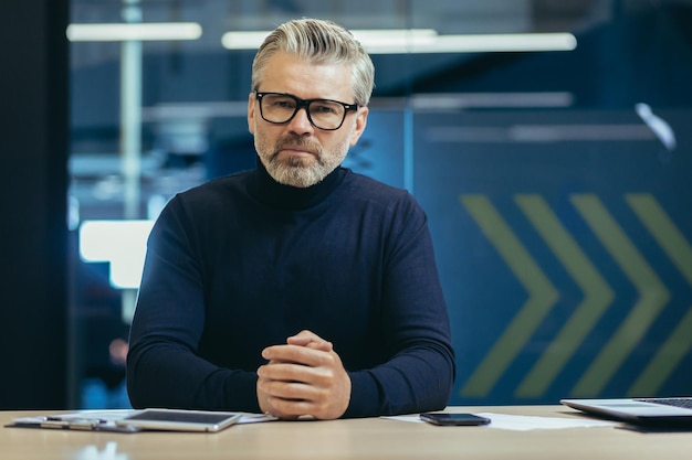 Retrato de un hombre mayor de pelo gris con gafas de un entrenador de profesores que se sienta seriamente en