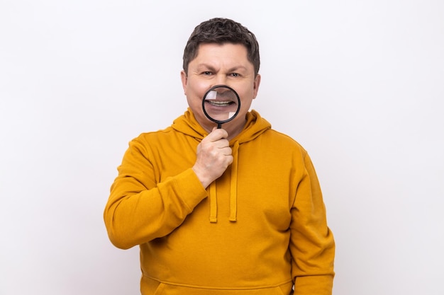 Retrato de un hombre de mediana edad de pie sosteniendo una lupa en sus dientes mirando con una sonrisa con dientes