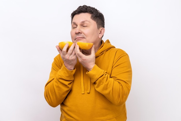 Retrato de un hombre de mediana edad que huele a media rodaja de pomelo disfrutando de una sabrosa fruta fresca y jugosa de vitamina