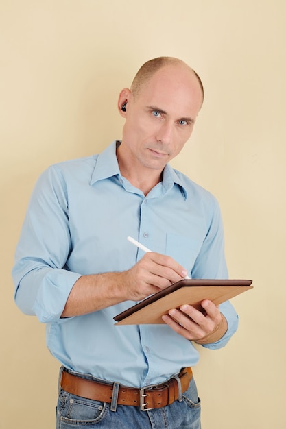 Retrato de hombre de mediana edad serio escribiendo o dibujando en una tableta con lápiz digital y mirando a la cámara