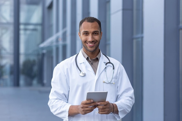 Retrato de hombre médico hispano feliz y sonriente sonriendo y mirando a la cámara médico usando tableta