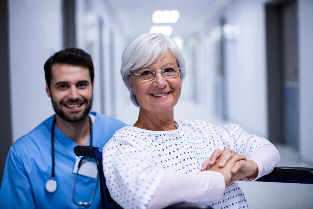 Retrato de hombre médico y paciente senior femenino sonriendo en el pasillo