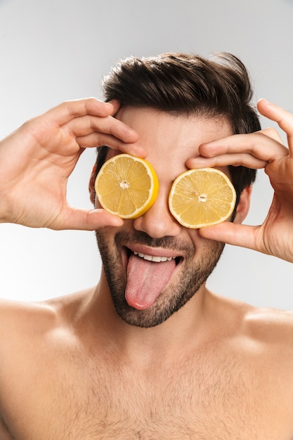 Retrato de hombre medio desnudo alegre riendo y burlándose con limón aislado en blanco