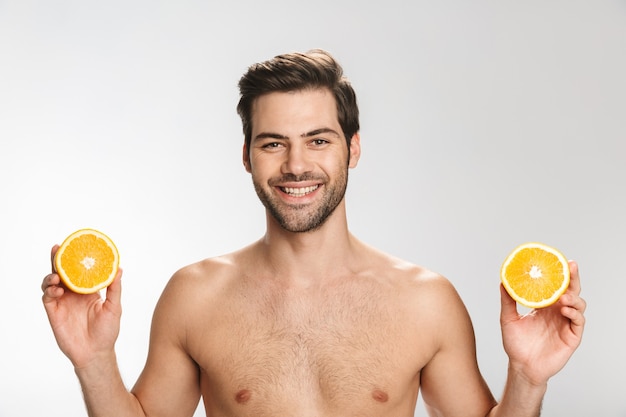 Retrato de hombre medio desnudo alegre sonriendo y sosteniendo naranja aislado en blanco