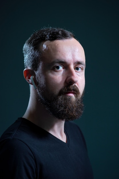 Retrato de un hombre milenario barbudo con auriculares inalámbricos en un fondo oscuro