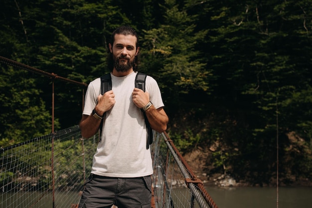 Foto retrato de un hombre con una mochila de pie en un puente peatonal contra el bosque