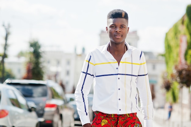 El retrato del hombre modelo afroamericano elegante hermoso en pantalones rojos y la camisa blanca presentó en la calle.